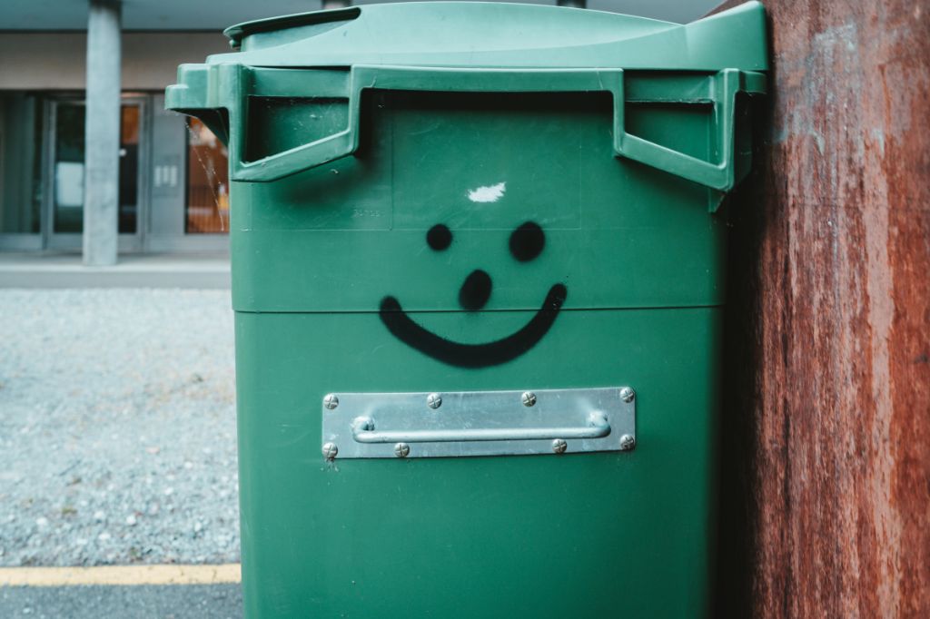 image of a green plastic trash can with a smiley face painted on the side